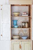 Vintage kitchen cupboard with wallpapered back wall, open door and view of crockery