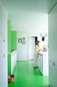 Woman in open-plan white, designer kitchen with green floor
