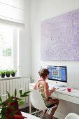 Mädchen auf weißem Schalenstuhl vor Computer im Jugendzimmer mit modernem Flair