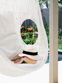 Sunhat and book in white, wicker hanging chair with cushions