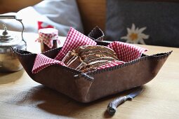 Red and white gingham napkin and sliced bread in rustic bread basket of stitched leather