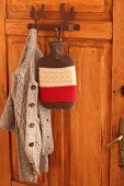 Cardigan and hot water bottle with felt and knit cover on coat pegs on wooden door