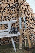 Vintage Skiausrüstung auf verwitterter Holzbank vor Brennholzstapel an Hauswand