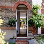 Arched doorway in brick facade of residential house and view of terrace seating area through open door