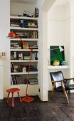 Red, metal standard lamp and red stool in front of fitted bookshelves next to open doorway and view of vintage armchair