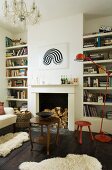 Sheepskin rugs on dark board floor and side table in front of open fireplace; red, retro standard lamp in front of bookcase