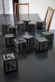Several alphabet blocks on dark table top and fifties-style chairs