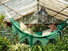 Hammock with scatter cushions amongst plants in old greenhouse