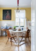 Traditional Bavarian board chairs at round, white dining table and collection of blue and white china on console table below old oil painting