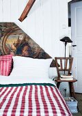 Piece of old wooden ceiling from demolished Baroque church used as artistic headboard of double bed with rustic, gingham bedspread and board chair used as bedside table