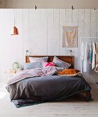 Modern, wooden double bed with reversible bed linen against white-painted wooden wall
