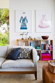 Comfortable designer sofa with scatter cushions, framed fashion illustrations and wooden shelves against wall in background