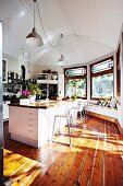 Light-flooded kitchen with wooden floor & retro pendant lamps hanging from white wooden ceiling above island counter