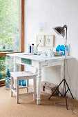 Weiß lackierter Holztisch mit gedrechselten Beinen und Hocker im Vintagelook neben Retro Stehleuchte aus Metall in Zimmerecke
