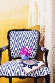 Postmodern chair with white and blue upholstery and black wooden frame against yellow wall draped in lace fabric