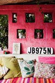 Masonry sofa with scatter cushions in front of pink external wall with ornaments in niches and car registration plate