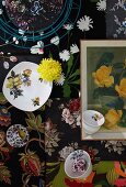 Top view of cups, plates, yellow flowers and framed picture on floral fabrics