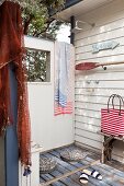 Aussendusche an holzvertäfelter Wand mit umfunktioniertem Holzpaddel und maritimem Streifendessin auf Badetasche und Handtüchern
