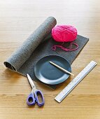 Roll of grey felt, ball of pink wool, plate, scissors and ruler