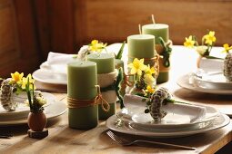 Row of green candles amongst place settings with Easter decorations