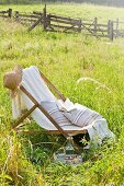 Deckchair, straw hat, cushions and book in summer meadow