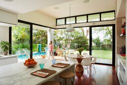 Place mats on counter in modern, open-plan interior with view of pool in garden