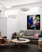 Sofaecke mit Designermöbeln und buntem modernem Wandbild neben weisser Trennwand