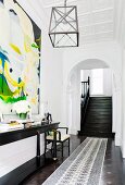 High-ceilinged entrance area with stucco ceiling and staircase leading through arched doorway; large modern painting on wall above narrow, black, antique console table