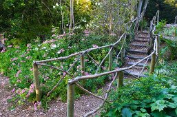 Kiesweg mit Geländer aus Holz in blühendem Garten
