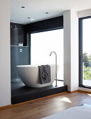 Puristische Bad Ensuite mit freistehender weißer Designer Badewanne auf schwarzem Podest mit Duschbereich