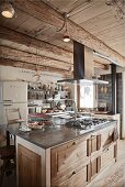 Rustic island counter with stainless steel extractor hood in open-plan interior of wooden chalet