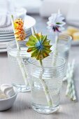 Colourful paper rosettes on drinking straws in glasses