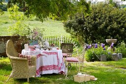 Gedeckter Tisch für den Nachmittagstee mit verschiedenen, alten Stühlen in romantischem Garten