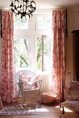 Weisser Korbstuhl vor Fenster mit bodenlangen Vorhängen im traditionellen Schlafzimmer