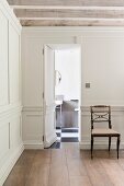 Door hidden in white wooden wall panelling opens to show guest bathroom in minimalist, elegant country-house hallway
