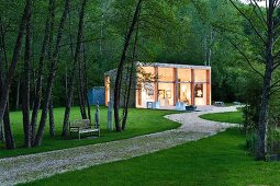 Contemporary studio building with terrace in idyllic grounds of old mill in the Dordogne; bench and sculptures next to path below trees
