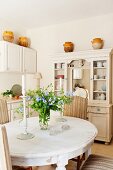 Dining room with country-house-style ceramic pots on dresser and candlesticks and flowers on oval dining table