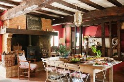 Large kitchen-dining room in French country house with old wood-beamed ceiling and log burner