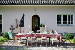 Set table and delicate metal chairs on gravel terrace in garden adjoining rustic house
