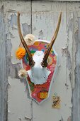 Antlers painted white on shield covered in Chinese wrapping paper, garland of everlasting flowers and postage stamp on old wooden door with peeling paint