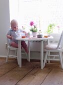 Baby sitting at table on child's chair eating tart
