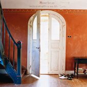 Hauseingang mit blauer Treppe neben Flügeltür mit Rundbogen und rotbrauner Wand mit Schablonenmalerei in altem Landhaus