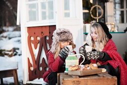Zwei Mädchen winterlich eingepackt bei wärmender Teepause vor skandinavischem Gartenpavillon