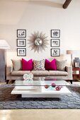 Sunburst mirror and black and white photographs above grey couch; crystal and glass ornaments on coffee table