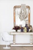 White tulip chair next to antique console table and hand-crafted pendant lamp in front of flyblown mirror