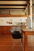 Schwarzer Schalenstuhl mit Metallgestell an Holztisch vor Küchenzeile in offenem Wohnraum