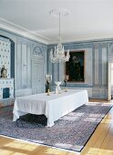 Herrschaftliches Speisezimmer mit bemalten Holzpaneelen an Wand und langer Tafel mit weisser Tischdecke unter Kerzenleuchter