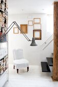 Books and storage boxes on steel shelving and chair with loose cover on white wooden floor; arrangement of picture frames and floating staircase in background