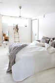 Doppelbett mit hellgrauem, gestricktem Plaid in skandinavischem Schlafzimmer mit weißem Dielenboden; im Hintergrund Dekoleiter und Standspiegel