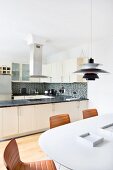 Leather chairs at white table below Poulsen pendant lamp in front of open-plan fitted kitchen with U-shaped counter